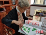 93岁高龄的民间剪纸艺术家、国家级非遗传承人袁秀莹正在翻阅她的作品集。叶秋云 摄 - 福建新闻
